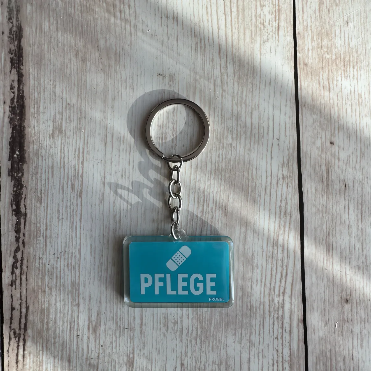 Acryl-Schlüsselanhänger "Pflege" mit Pflaster-Symbol